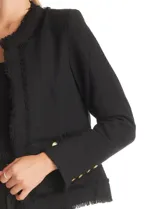 Chaqueta de tweed estructurada con cuello a la base, corte recto y largo a la cintura. Presenta terminaciones deshilachadas en los bordes, bolsillos frontales y botones metálicos dorados decorativos en puños y bolsillos.
