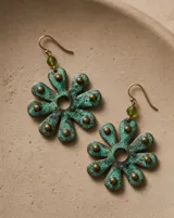 Aros colgantes con diseño de flor de ocho pétalos en cobre oxidado con pátina turquesa y detalles de tachas metálicas. Incluye pasante de plata esterlina y una pequeña cuenta de cristal verde en la parte superior.