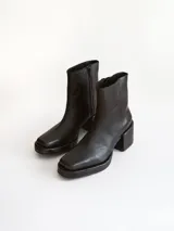 Bota corta de cuero negro con punta cuadrada y taco bloque texturizado. Presenta cierre lateral y costura central en el empeine.