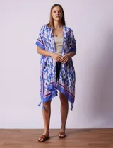 Kimono tejido con estampado abstracto en tonos azules, blancos y violetas. Tiene terminación de ruedo con borlas.