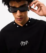 Remera boxy negra de algodón con cuello V decorado con pequeñas estrellas bordadas y un bordado numérico en el centro del pecho.