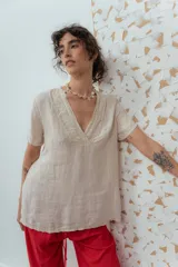 Blusa de lino color beige de calce relajado, con escote en V y detalles de pliegues frontales. Posee mangas cortas y una silueta suelta.