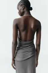 Vestido largo de color negro con cuello halter y detalle de aro metálico en el escote. Presenta un diseño drapeado en la parte frontal y escote en pico pronunciado.