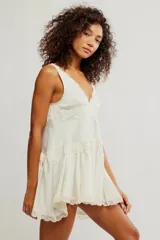 Mini vestido tipo slip de tela satinada negra, con escote en V profundo, diseño en capas con volados y detalles de encaje en los bordes. Corte estilo babydoll, sin mangas y silueta amplia.
