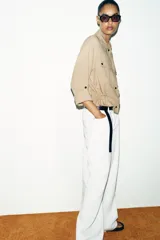 Chaqueta corta marrón de cuello solapa y manga remangada por debajo del codo. Presenta bolsillos delanteros de plastrón con solapa, bajo ajustable con cordón interior y cierre frontal con botones.