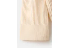 Jersey de punto color marfil con cuello alto y bufanda integrada del mismo tejido y textura acanalada, de diseño holgado y manga larga.