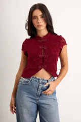 Top bordó de encaje elastizado, con cuello mao y cierre frontal con broches anudados tradicionales. Presenta mangas cortas y diseño corto al cuerpo.