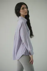 Camisa de rayas verticales rosadas y celestes, con cuello clásico, botonadura frontal y doble bolsillo delantero. Tiene un calce relajado y terminación curva en el ruedo.