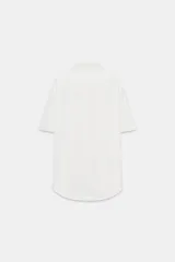 Camisa de cuello solapa y manga corta, confeccionada en tejido satinado. Presenta falsos bolsillos con solapa en el delantero, bajo asimétrico y cierre frontal con botones.