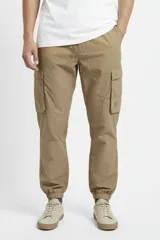 Pantalón cargo de nylon color beige, con elástico en la cintura y en los puños. Presenta bolsillos laterales con solapa y un logo de goma aplicado en uno de ellos.