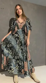 Vestido largo con escote en V tanto en el frente como en la espalda, mangas cortas amplias y corte elastizado debajo del busto. Presenta un estampado de estilo paisley y guardas geométricas en tonos azules, negros y corales.