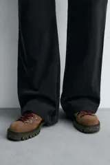 Zapato de cordones estilo trekking para hombre, confeccionado en piel con acabado de serraje color marrón. Presenta enganches metálicos para los cordones, cuello acolchado en color negro y una suela de goma con volumen y efecto moteado.