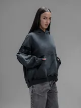 Hoodie oversize de corte crop en color gris oscuro, confeccionado en algodón rústico. Presenta un diseño con costuras expuestas, efecto de desgaste y detalles de roturas en los bordes, incluyendo puños y ruedo.