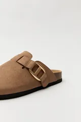 Zueco de estilo casual con capellada cerrada en material tipo gamuza color negro. Presenta una hebilla metálica decorativa en tono dorado sobre el empeine y una base anatómica con efecto corcho.