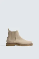 Bota estilo Chelsea de hombre, confeccionada en piel con acabado de serraje en color beige. Presenta elásticos laterales al tono, horma redonda y suela de goma a contraste con ligero tacón.