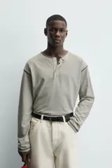 Camiseta de manga larga con cuello panadero (henley) y cierre de tres botones. Presenta un patrón de rayas horizontales finas en tonos beige y negro, con pespuntes a contraste en el cuello, puños y bajo.