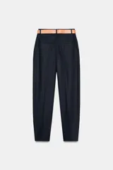 Pantalón tobillero azul marino de tiro medio, con pinzas delanteras, bolsillos frontales, falsos bolsillos con solapa en la espalda y cierre frontal con cremallera, botón y gancho. Incluye cinturón de cuero sintético tostado con hebilla metálica dorada.