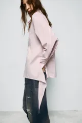 Camisa de corte oversize con cuello solapa y escote en pico. Presenta manga larga con puños abotonados, cierre frontal con botones y detalle de lazada ajustable en la espalda.
