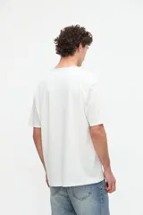 Remera blanca de algodón con textura suave, corte relaxed, manga corta, cuello redondo en contraste de color celeste y un bolsillo aplicado en el pecho.