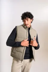 Chaleco puffer de corte regular, color beige, con cierre frontal y cuello alto. Presenta un diseño acolchado horizontal y logo bordado en el pecho.