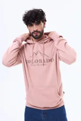 Buzo tipo canguro con capucha y cordones ajustables, confeccionado en felpa color rosado. Presenta un estampado frontal con diseño de montañas y el texto 'COLORADO Rocky Mountain'. Cuenta con bolsillo frontal tipo canguro y puños acanalados.