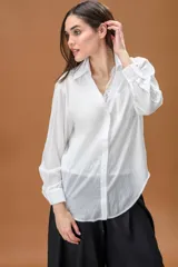 Camisa blanca de corte clásico con cuello camisero, manga larga y bolsillo frontal, que incluye una musculosa interior con detalle de encaje visible en el escote.
