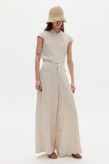 Pantalón ancho color beige confeccionado en lino 100% natural, de tiro medio-alto con elástico interno en la cintura, cierre frontal con gancho y bolsillos laterales.
