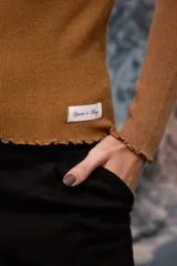 Polera de tejido de punto fino color blanco, con cuello alto, mangas largas y terminaciones con detalle de ondas en puños, cuello y ruedo.