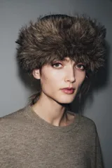 Gorro de estilo ruso con parte superior de cuero sintético negro y borde ancho de piel sintética en color marrón. Presenta costuras marcadas en la parte superior.