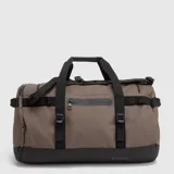 Bolso tipo duffel de diseño versátil, color marrón con detalles en negro. Cuenta con compartimento principal amplio, bolsillos exteriores con cierre, asas de mano y correas ajustables para usar como mochila.