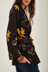 Saco tipo kimono de satén negro con estampado floral en tonos violeta y amarillo, con lazo ajustable en la cintura y mangas largas.