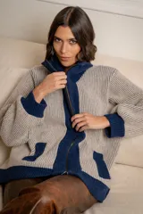 Campera de punto tipo cárdigan con cierre frontal de doble cursor, confeccionada en lana. Presenta un diseño bicolor con cuerpo en tono gris claro y detalles en azul marino en el cuello, la franja central, los bolsillos y los puños. Posee mangas largas con terminación ajustada y bolsillos frontales.
