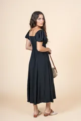 Vestido midi de color negro, con escote cuadrado, mangas cortas abullonadas y detalle de frunces con lazo en el centro del pecho. Presenta una silueta entallada en la cintura y falda con caída fluida.