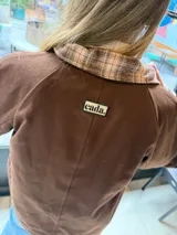 Campera reversible de corte holgado con cuello alto. De un lado presenta un diseño a cuadros en tonos marrones y beige, y del otro lado un diseño liso. Cuenta con cierre frontal de botones y mangas largas.