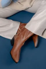 Bota de caña media color chocolate, confeccionada en cuero con textura granulada. Presenta un diseño de estilo western con punta fina, taco cuadrado y una tira lateral decorada con tachas metálicas circulares en tono bronce.