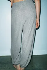 Pantalón de tiro alto confeccionado en tejido de punto mezcla de algodón, con cintura elástica y detalle de botones frontales. Presenta un diseño de pernera amplia con bajo abullonado acabado en elástico.