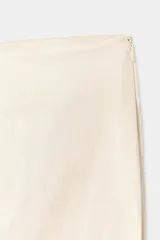 Falda midi recta de tiro medio confeccionada en tejido satinado color beige, con abertura en la espalda y cierre lateral con cremallera oculta.