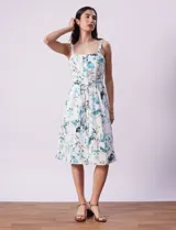 Vestido midi blanco con estampado floral celeste y verde, escote recto con tirantes, abertura frontal con botones, lazo en la cintura y bolsillos laterales.