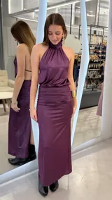 Vestido largo color lila con acabado brillante, escote halter y diseño drapeado en la zona de la cintura.