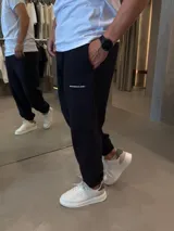 Pantalón de jogging negro de algodón premium, con cintura elástica, bolsillos laterales y puños elastizados en los tobillos. Presenta pequeño estampado tipográfico en la pierna izquierda.
