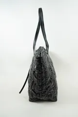 Cartera tipo shopper de color negro, con diseño acolchado y costuras cuadradas. Cuenta con doble asa larga para llevar al hombro y cierre superior.