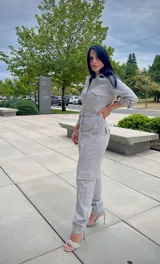 Mono largo gris con textura arrugada, cuello camisero, cierre frontal, bolsillos con solapa en el pecho y bolsillos cargo en las piernas. Incluye cordón ajustable en la cintura y mangas 3/4 con botón.