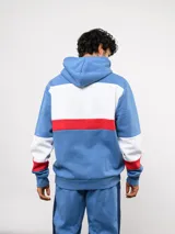Canguro con capucha de Umbro del Club Nacional de Football, con diseño de bloques de color en azul, blanco y rojo. Presenta bolsillo frontal tipo canguro, cordones ajustables en la capucha y logos bordados del club y la marca.