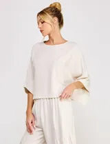 Blusa corta color beige de lino y viscosa, con escote redondo, mangas tres cuartos estilo kimono y corte holgado.