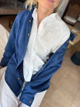 Camisa de manga larga confeccionada en popelina natural, con cuello clásico y cierre frontal de botones. Presenta un delicado bordado floral a tono sobre el hombro, aportando textura y un diseño minimalista.