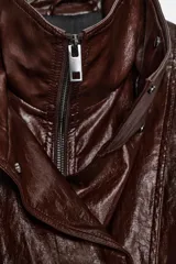 Chaqueta amplia de efecto piel en color marrón oscuro, con cuello alto, manga larga y bolsillos delanteros. Presenta cintura ajustable, forro interior y cierre frontal con cremallera y botones ocultos por solapa.