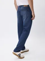 Jean de corte regular fit con tiro medio, confeccionado en denim de lavado oscuro con efecto localizado. Cuenta con diseño de cinco bolsillos, cierre frontal con cremallera y botón.