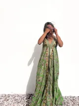 Vestido largo de estilo bohemio en color verde, con estampado paisley, escote en V profundo y breteles finos. Presenta detalles bordados con pedrería y espejos a lo largo del escote y el centro del frente, con una falda amplia y fluida.