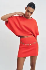 Top corto de punto color rojo coral, con cuello redondo y mangas cortas amplias con sisa ancha y costura central vertical.