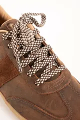 Zapatillas urbanas de cuero color marrón, con cordones estampados en tonos marrones y blancos, y suela de goma al tono. Presentan una franja lateral de gamuza y detalles con la marca en dorado.